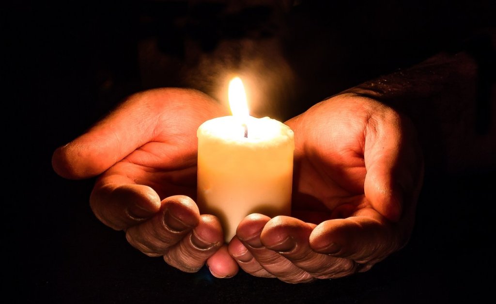 Hands cradling a candle in darkness
